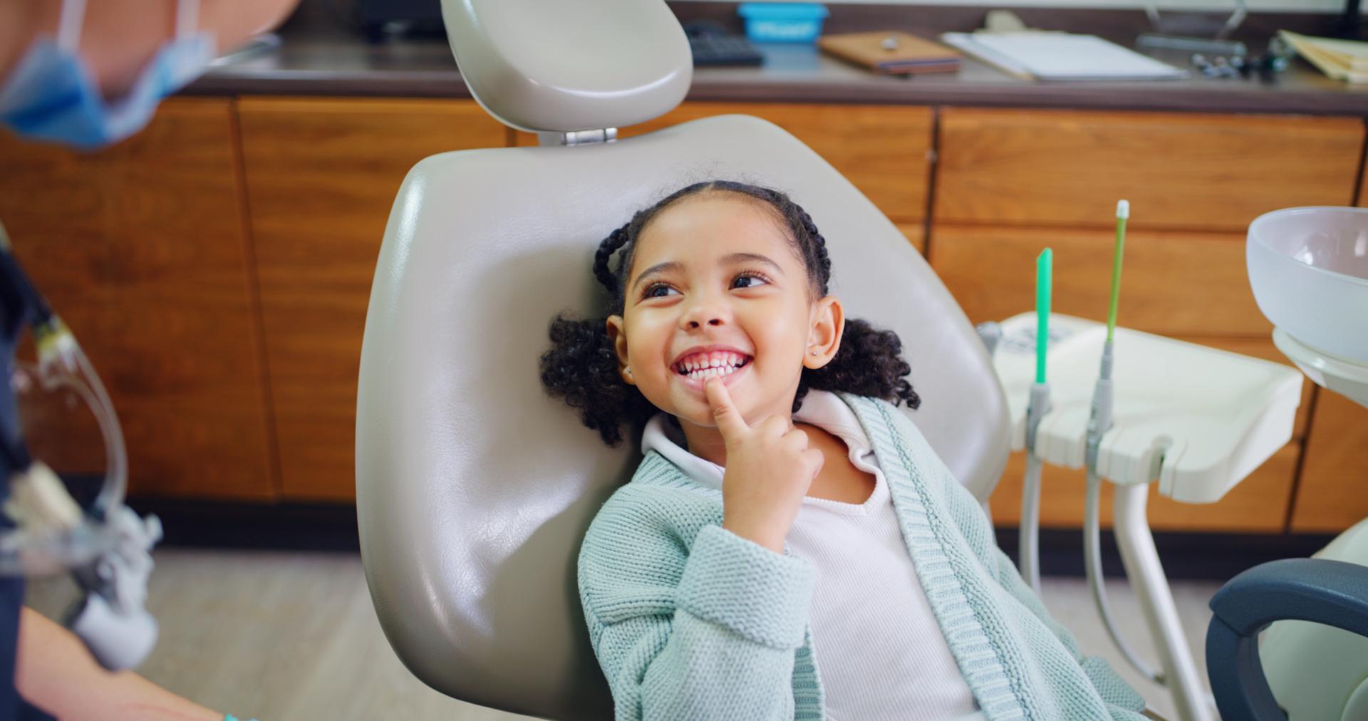 Young girl pointing to her smile in the dental chair